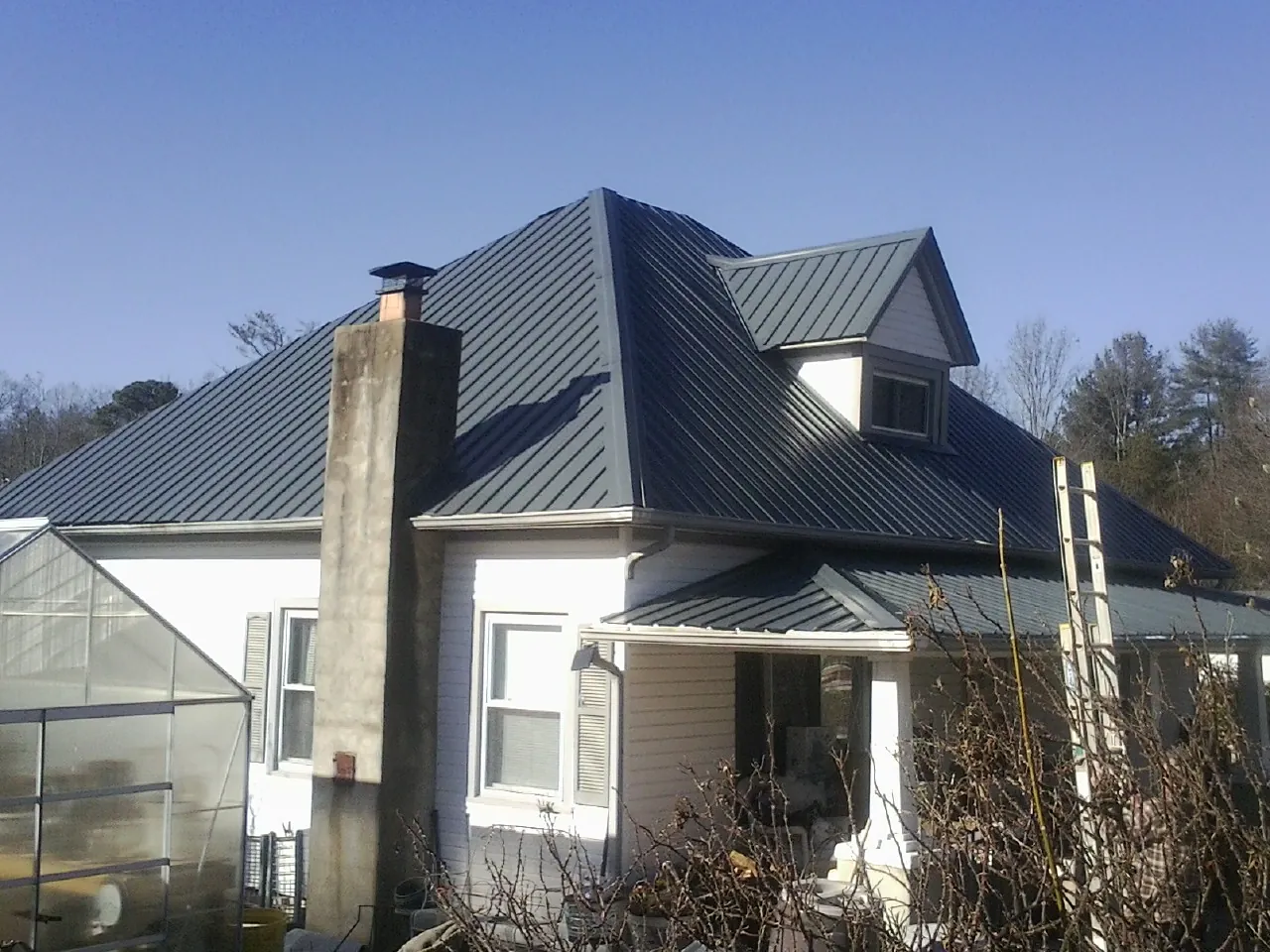 Dark blue standing seam metal roof on a white farmhouse with dormer — Slate & Tile Roof Repair by Roofing Brothers in Garden Prairie