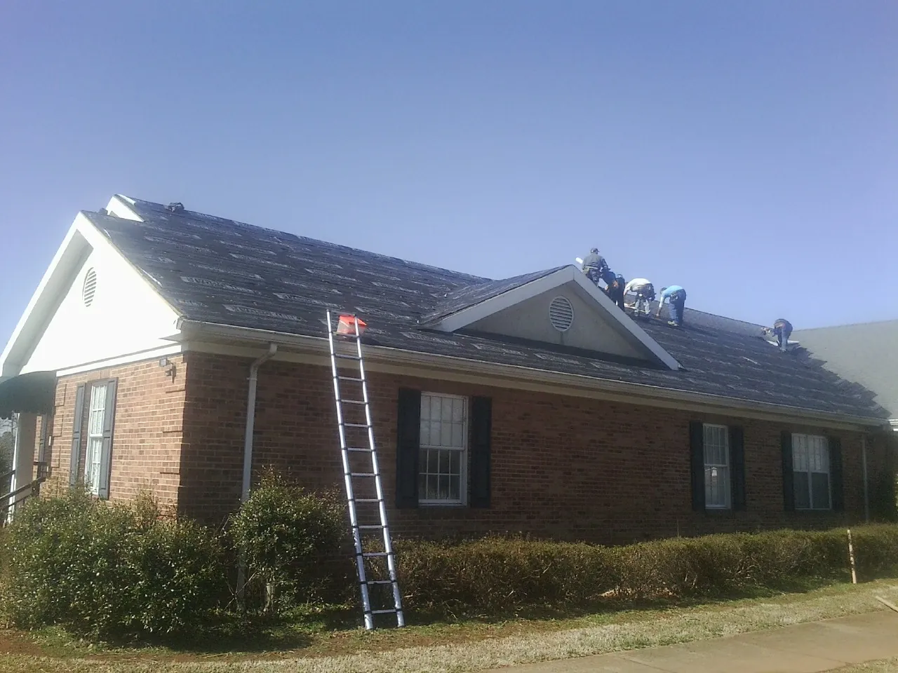 Crew tearing shingles off a brick ranch roof with a ladder set — Metal Roof Repair work by our crew in Garden Prairie