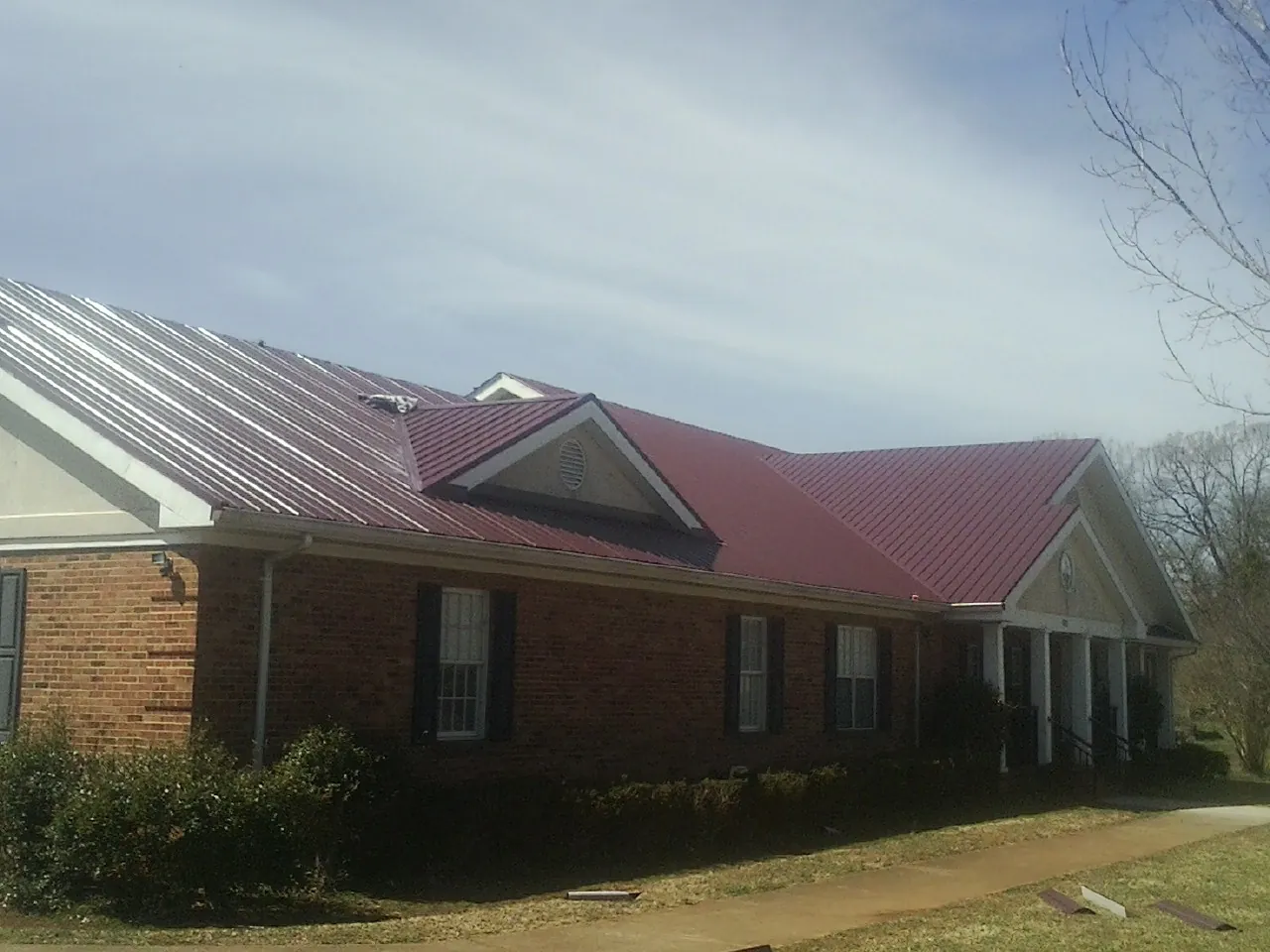 Red metal roof with gabled entries on a long brick building, from a Hail Damage Roof Repair job in Garden Prairie