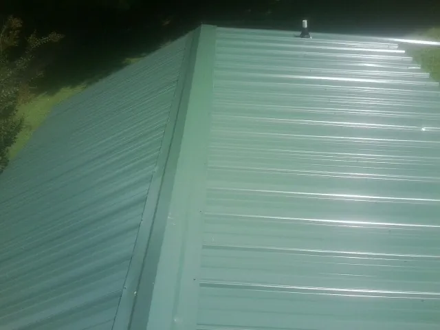 New green metal panels meeting at the ridge of a roof — Flat Roof Repair work by our crew in Garden Prairie