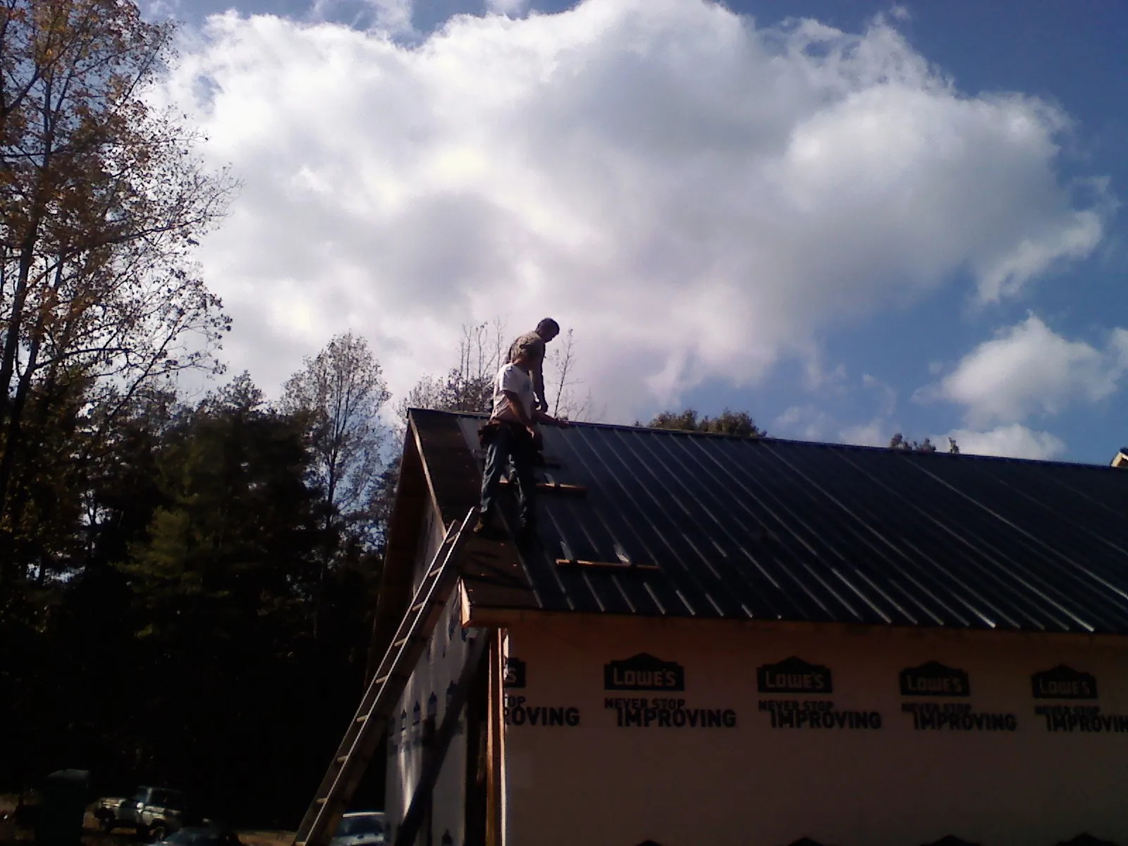Roofer fastening dark metal panels high against a cloudy sky, from a Roof Inspection job in Garden Prairie