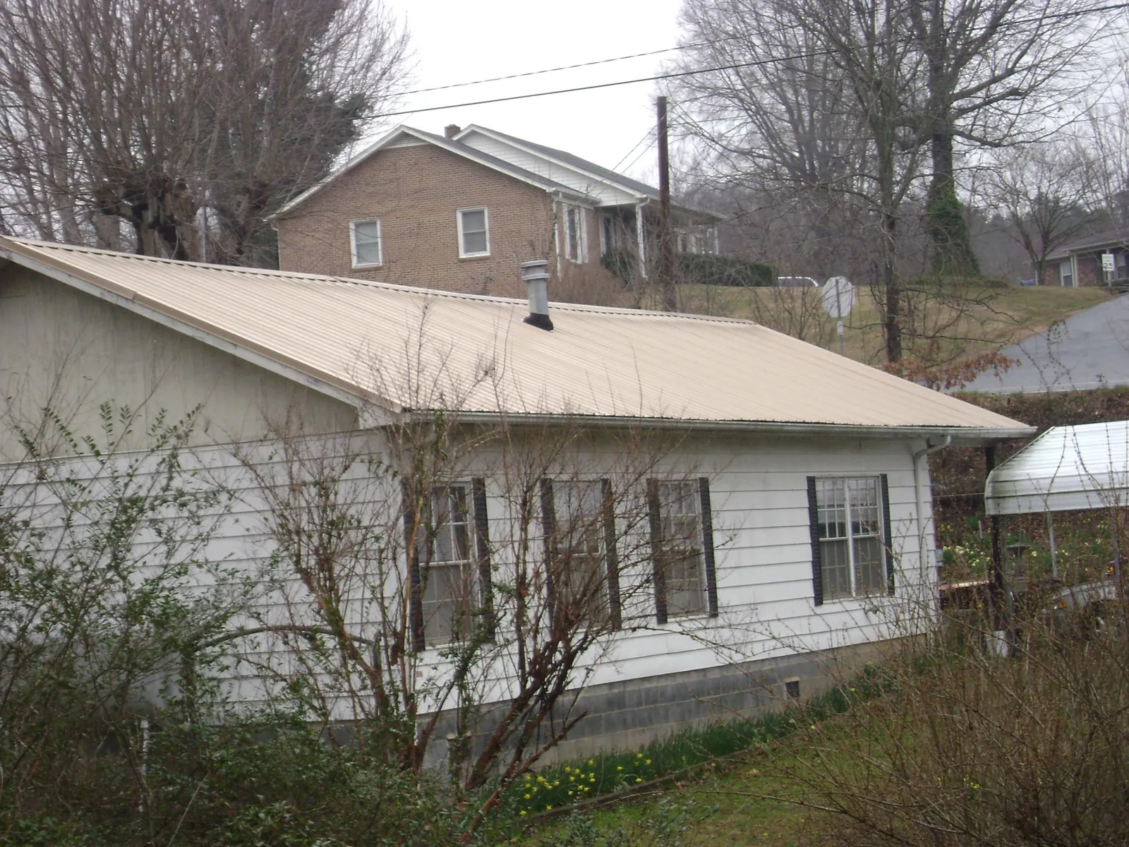 Tan metal roof on a white sided house set into a hillside — Commercial Roofing by Roofing Brothers in Garden Prairie