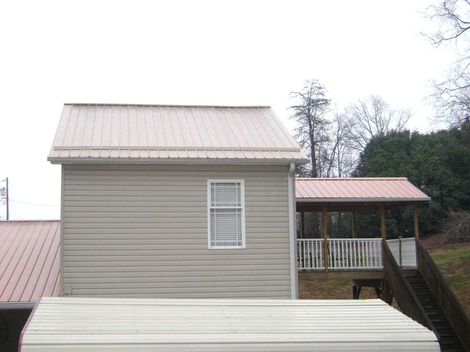 Tan metal roofs on a two story addition and attached porch, from a Roof Replacement job in Garden Prairie